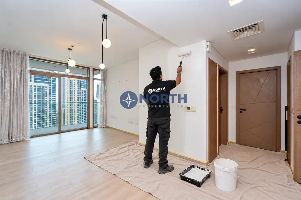 Painter rolling a living-area wall with the floor covered and skirting masked
