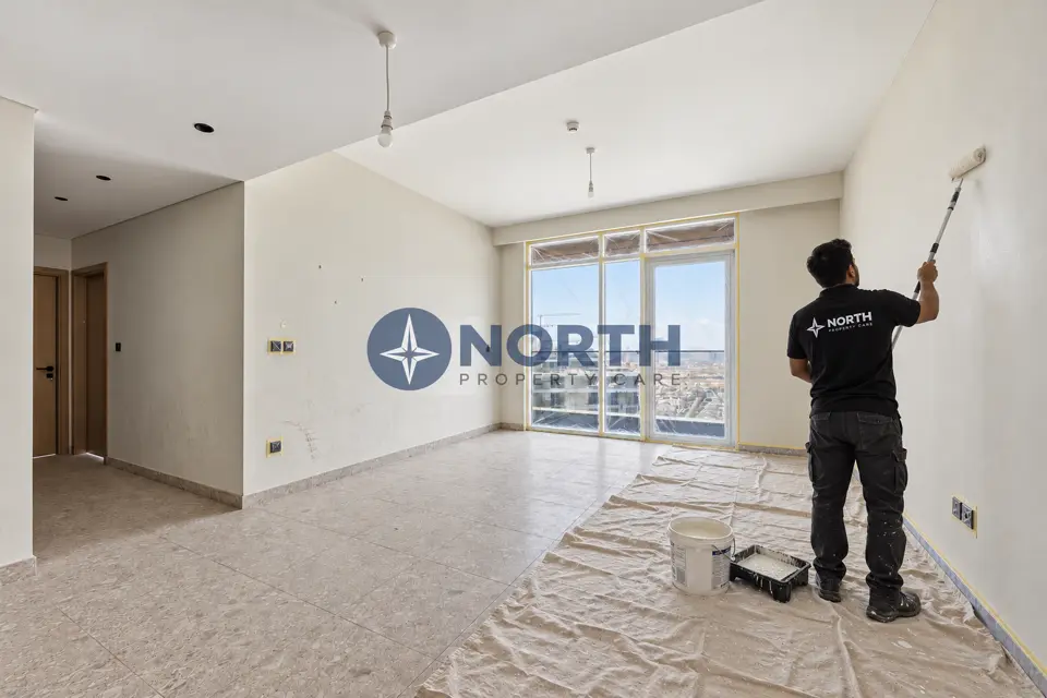 Painter rolling a Golf Suites living-area wall with the floor covered and window masked