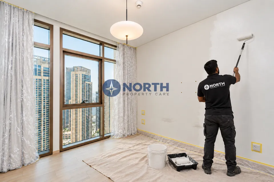 Painter rolling a bedroom wall with curtains wrapped, sockets masked and floor covered