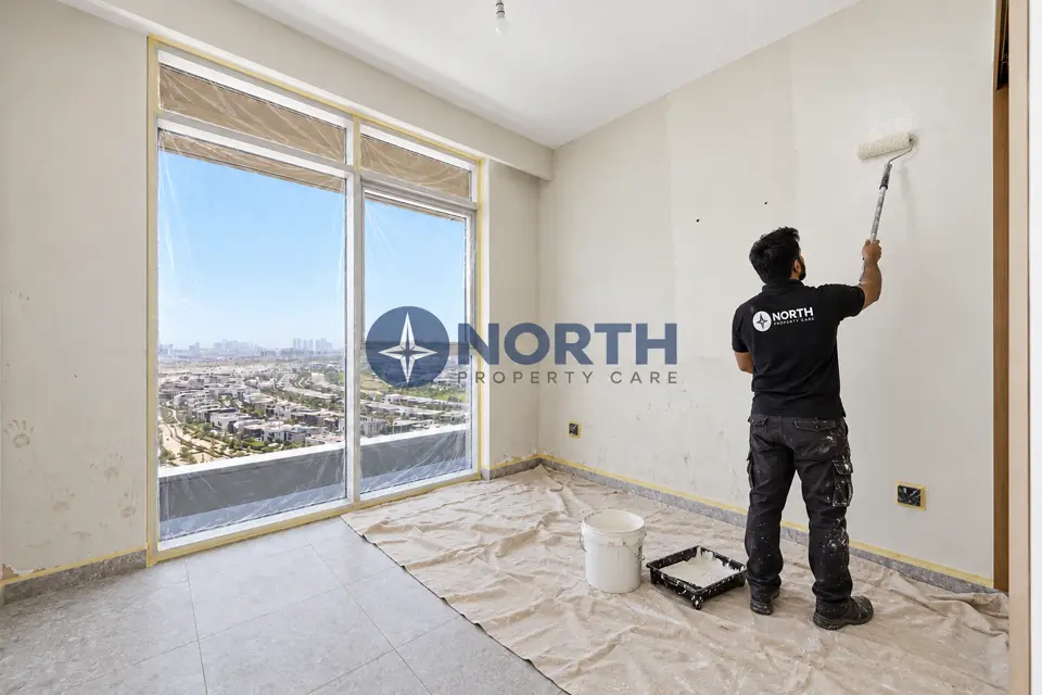 Painter rolling a Golf Suites bedroom wall with the floor covered and window masked