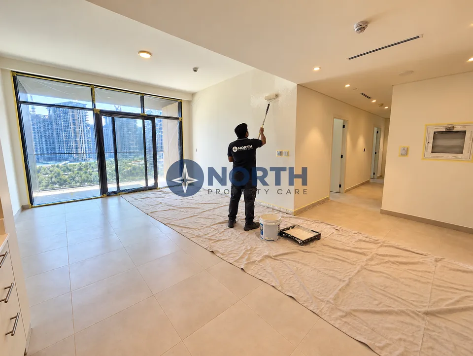 Painter applying wall paint in the Parkside Views living area facing the balcony, with the floor and glazing protected