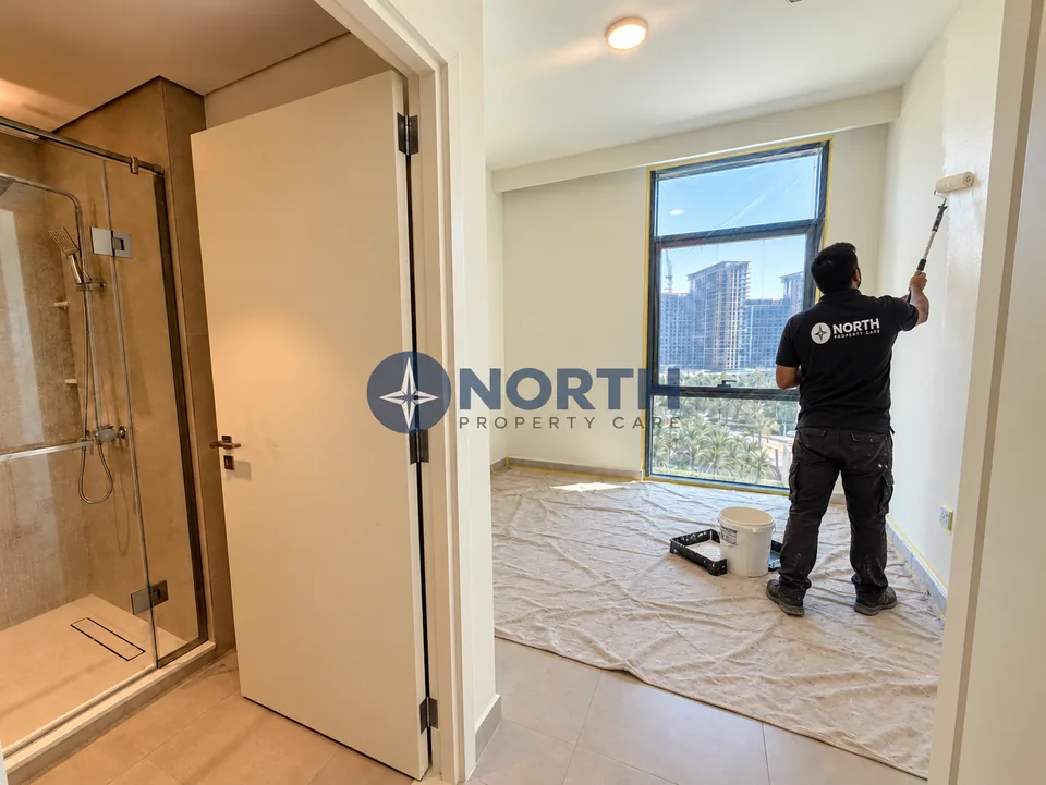 Painter applying wall paint beside the bedroom bathroom doorway at Parkside Views, with the floor and window protected